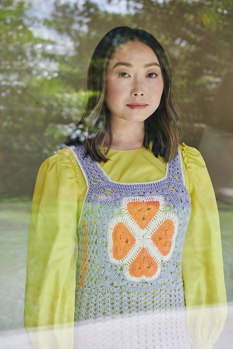 Vibrant portrait of young woman with dark hair and clear skin wearing colorful crochet top and yellow blouse, outdoor natural background, professional fashion photography by Pamela Hanson.