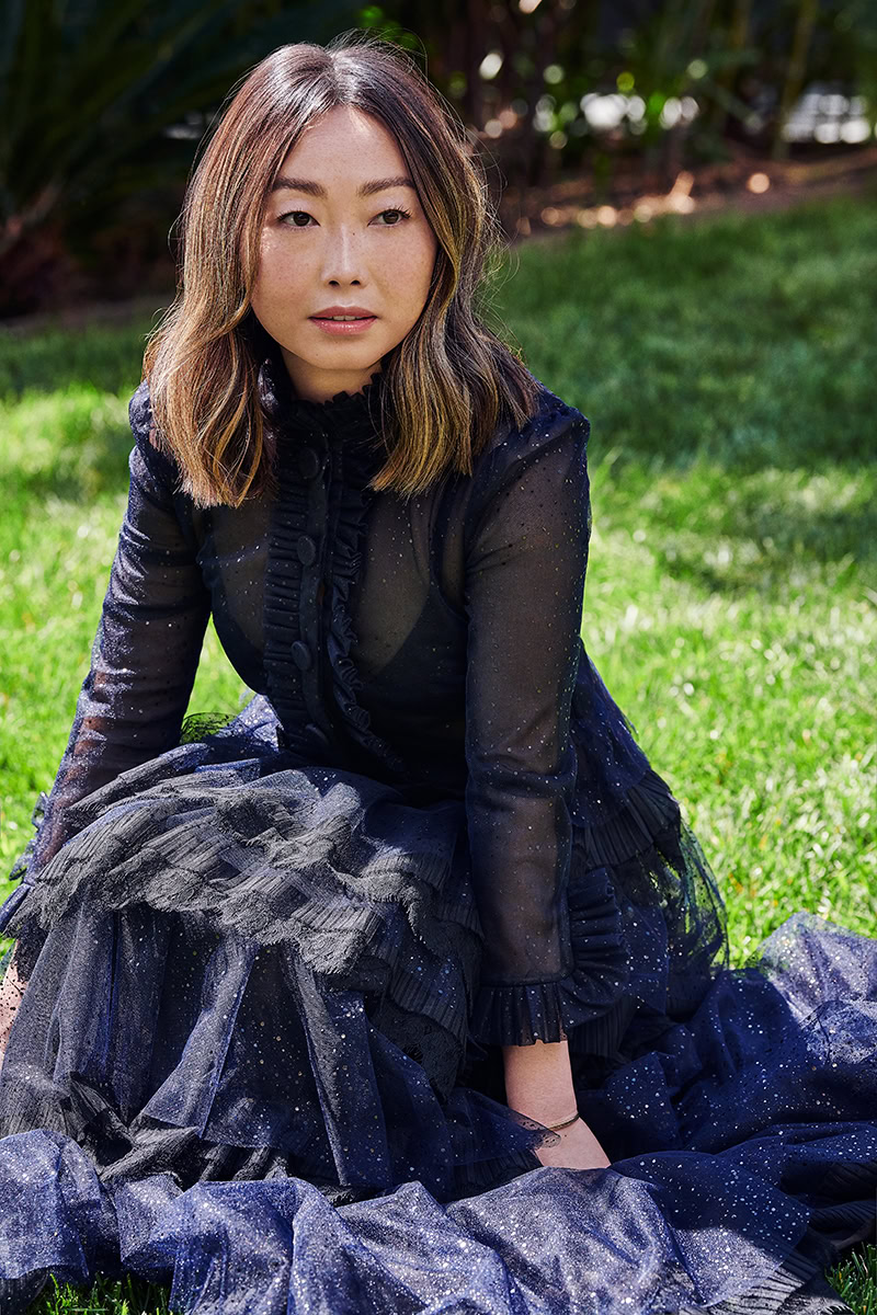 Elegant portrait of a woman in a dark, sparkly gown sitting on lush green grass in an outdoor setting for fashion and portrait photography by Pamela Hanson.