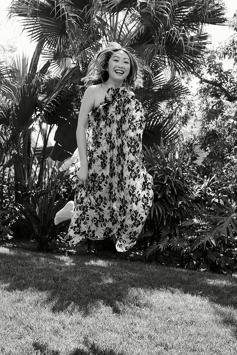Elegant floral dress fashion photography featuring a joyful woman outdoors surrounded by lush tropical plants, showcasing natural beauty and vibrant lifestyle moments.