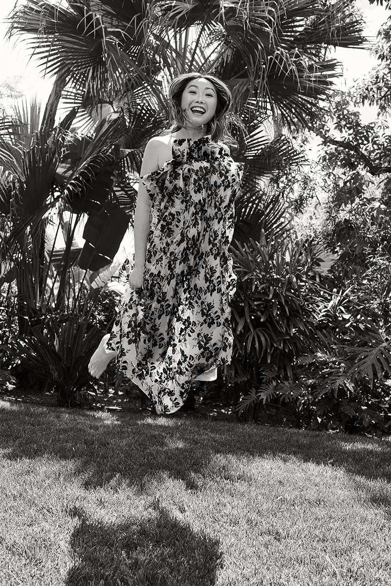 Vibrant black and white portrait of a joyful woman in a floral dress amidst lush tropical plants, captured by Pamela Hanson Photography for artistic and lifestyle photography.