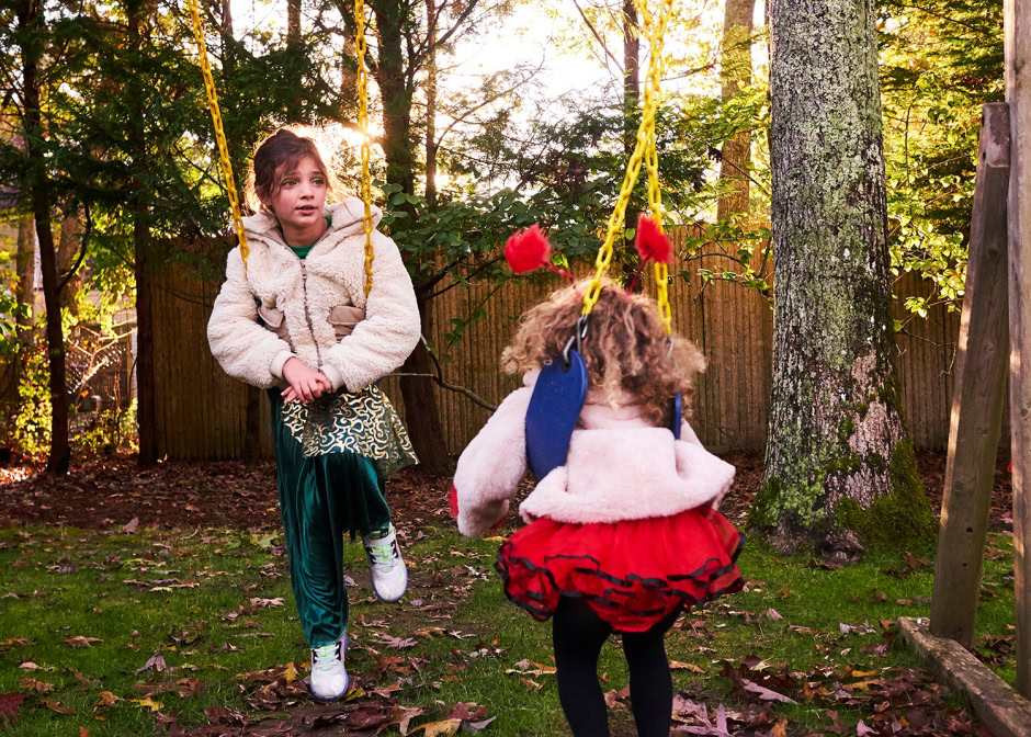 Colorful children playing on a swing set outdoors in a backyard during autumn, captured in warm sunlight, showcasing candid childhood moments and outdoor play.