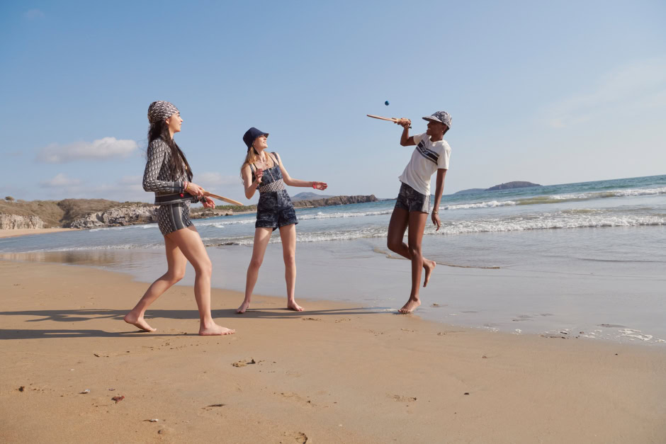 Youthful women playing with a ball on the sandy beach at sunset, stylish summer outfits, carefree fun, ocean waves, scenic coastal landscape, summer vacation, lifestyle photography, outdoor, nature backdrop.