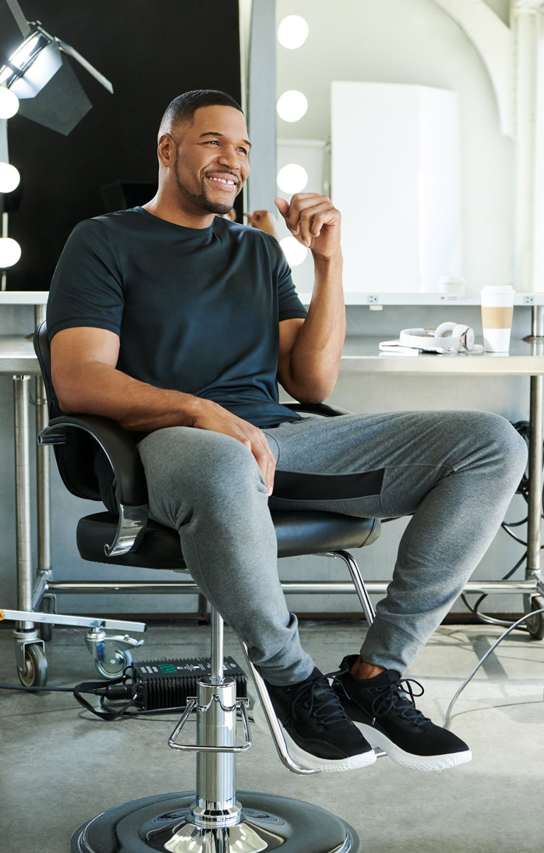 Happy man sitting in makeup chair at studio, professional photo shoot, confident smile, modern photography setting, Pamela Hanson Photography, beauty lighting, male model, portrait photography, creative studio shot, high-quality image, fashion and lifestyle photography, digital photography, editorial portrait.