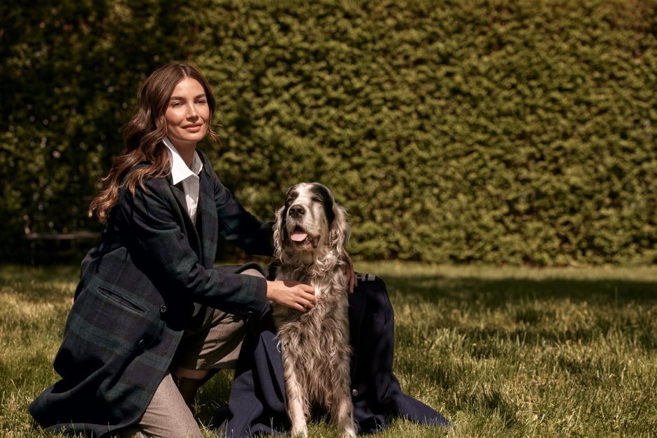 Stylish woman in a plaid blazer posing outdoors with her famous English Setter dog on a sunny day for Pamela Hanson Photography.