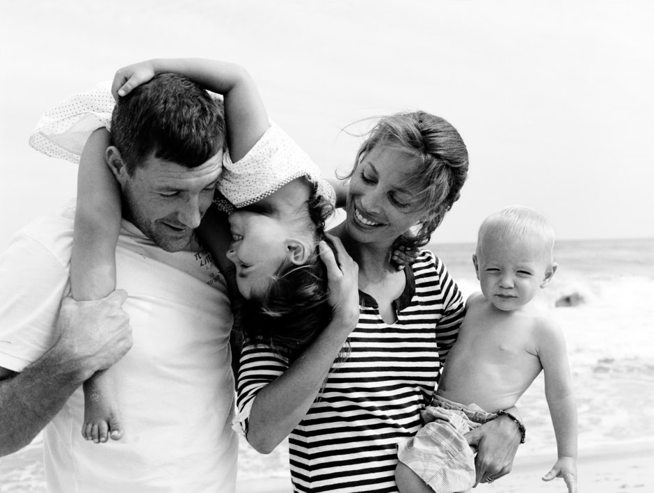 Family beach fun black and white photography showing parents with two children smiling and playing together on the seaside.