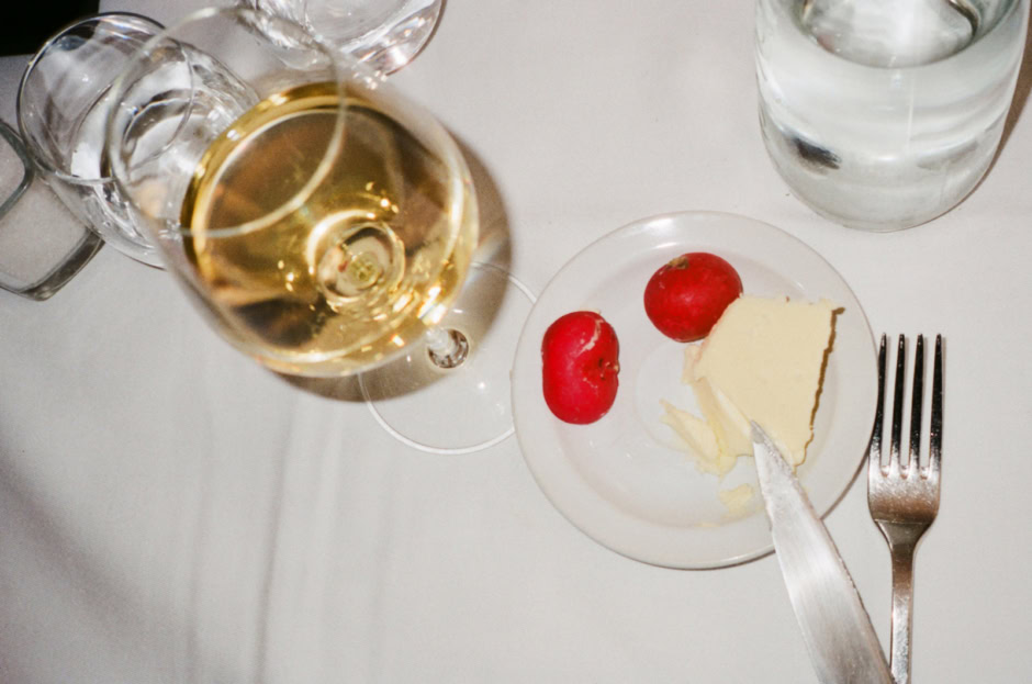 Elegant table setting featuring a glass of white wine, a slice of cheese, radishes, and water glasses on a white tablecloth. Perfect for showcasing sophisticated dining and lifestyle photography.