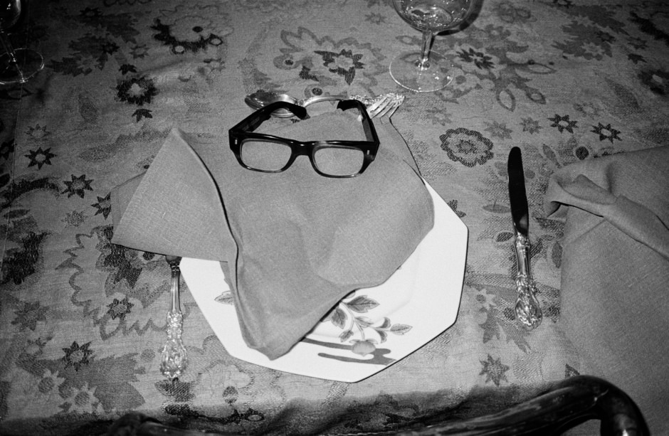Elegant table setting with a decorative napkin, black-rimmed glasses, and vintage-style cutlery on a floral tablecloth, showcasing fine dining details for wedding or event photography.