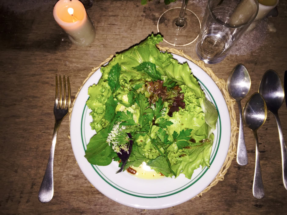 Fresh green mixed salad with leafy greens served on a white plate, surrounded by cutlery, candles, and glassware, captured in a cozy dining setting emphasizing healthy eating and gourmet presentation.