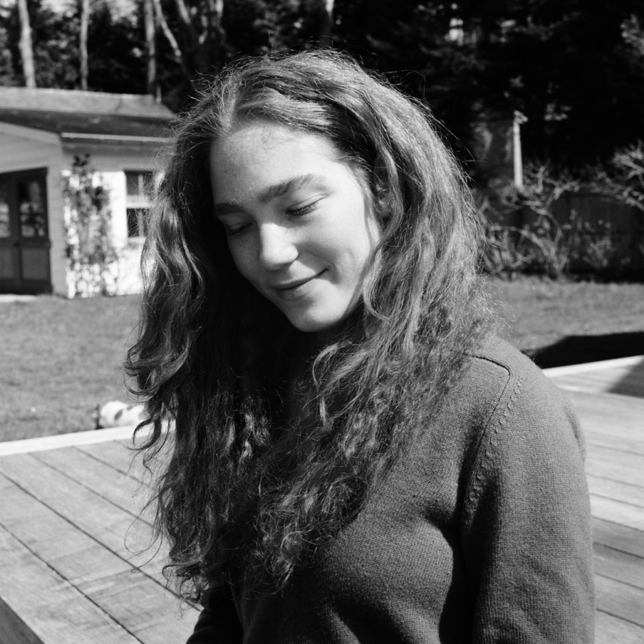 Black and white portrait of young woman with long wavy hair, outdoor natural light, artistic photography by Pamela Hanson Photography, serene and contemplative mood.