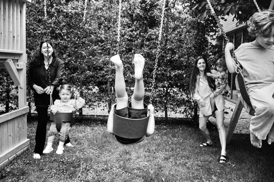 Children playing on swings in a backyard with trees and a fence.