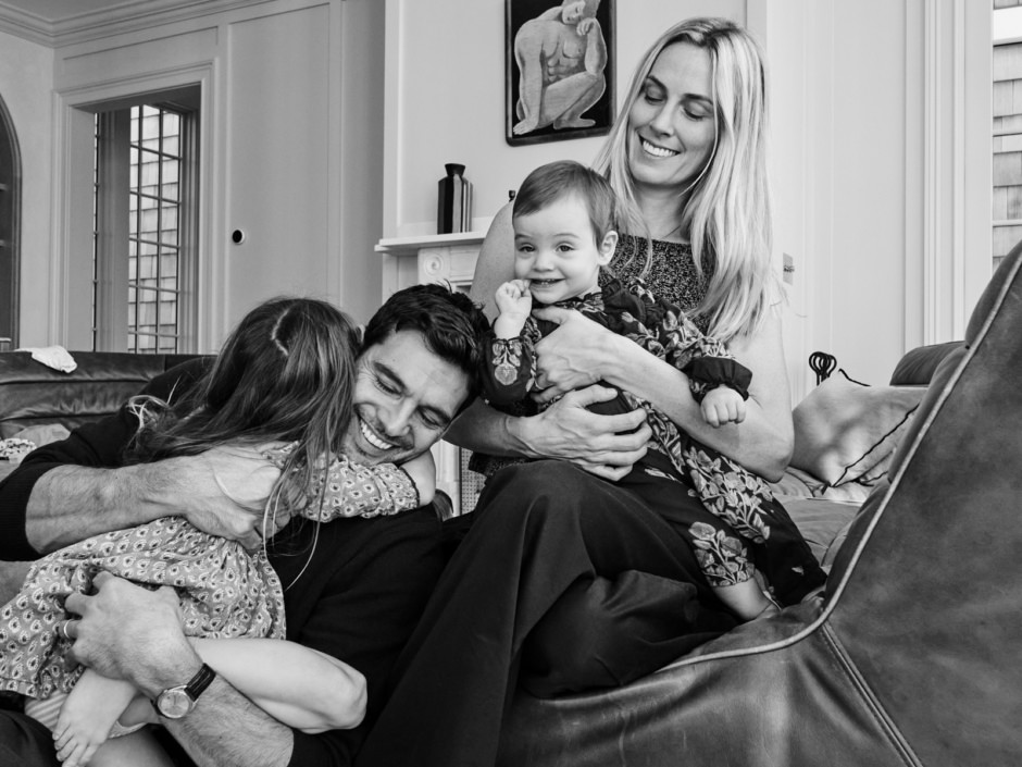 Joyful family moment with parents and children sharing a hug and laughter in a cozy living room, capturing authentic emotions for lifestyle and portrait photography by Pamela Hanson.