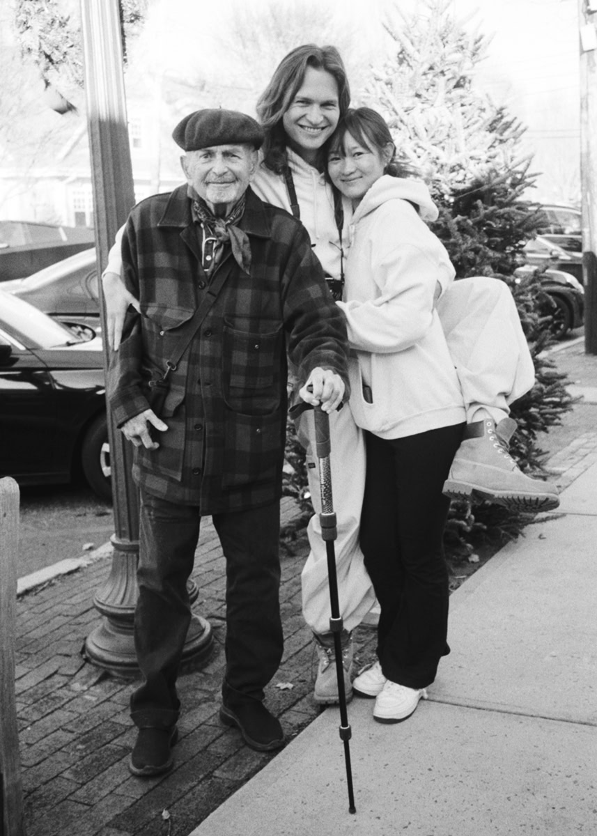 Smiling woman with two children standing outdoors near Christmas tree, family portrait, candid holiday moment, joyful family photography, black and white holiday scene.