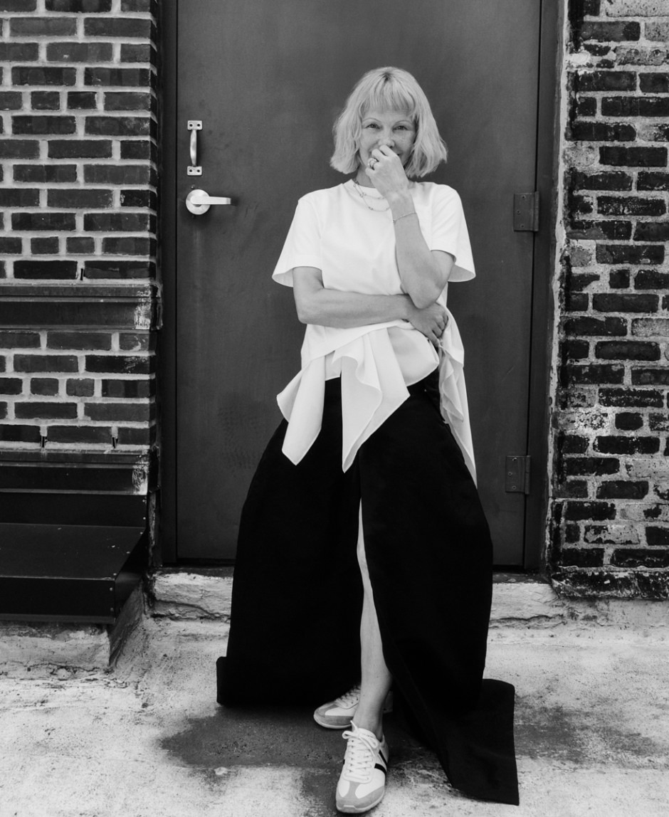 Funny woman in casual outfit laughing outdoors, urban brick wall background, black and white photography, candid street style, modern portrait photography capturing joyful expression and relaxed vibe.