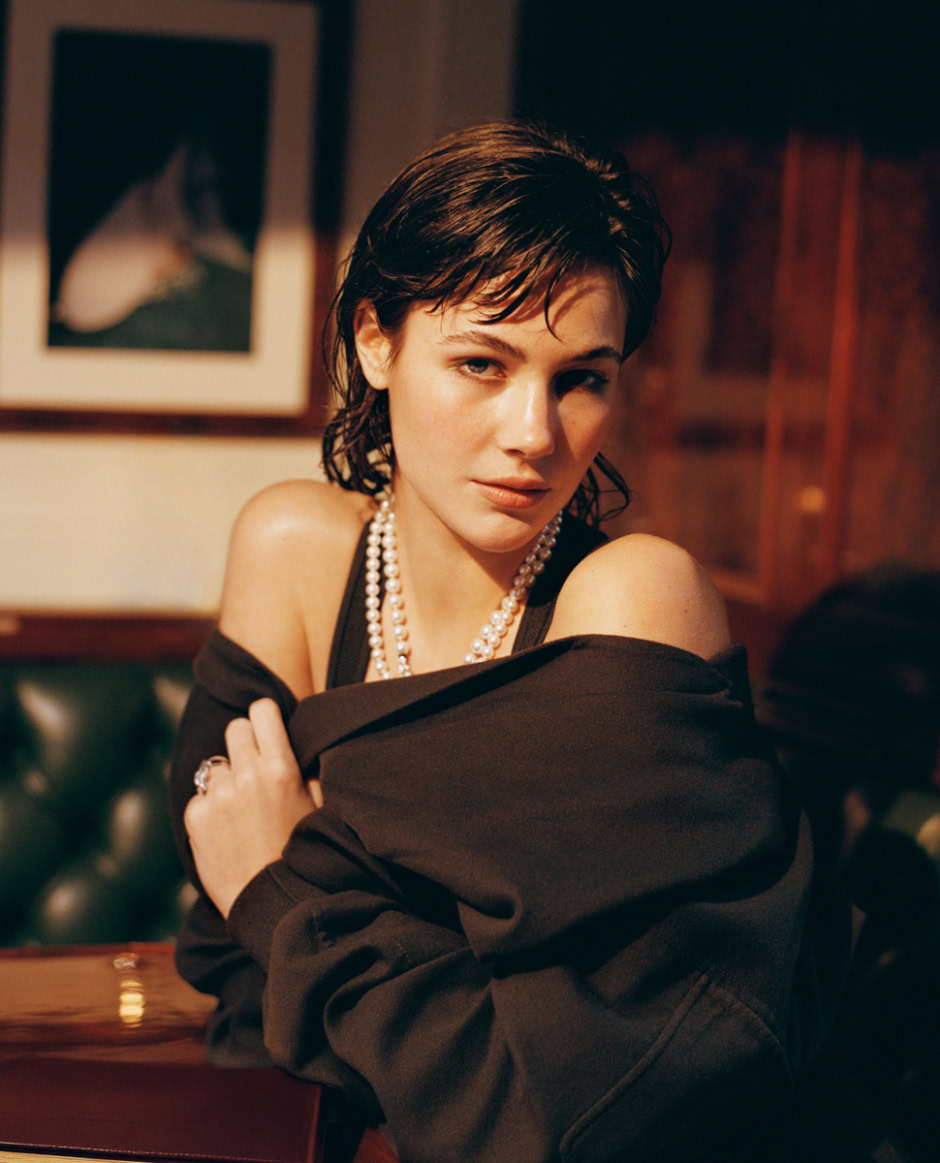 Black-haired woman wearing pearl necklaces sitting in a cafe, portrait photography, fashion, elegant style, warm indoor lighting, artistic portrait, Pamela Hanson Photography.