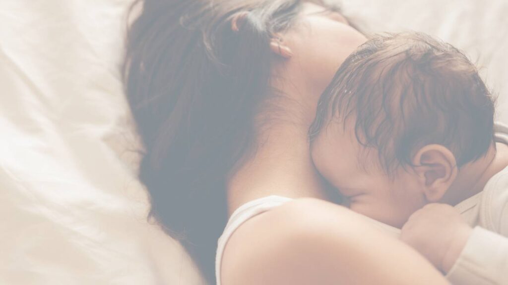 A mother lying down feeding her newborn in bed