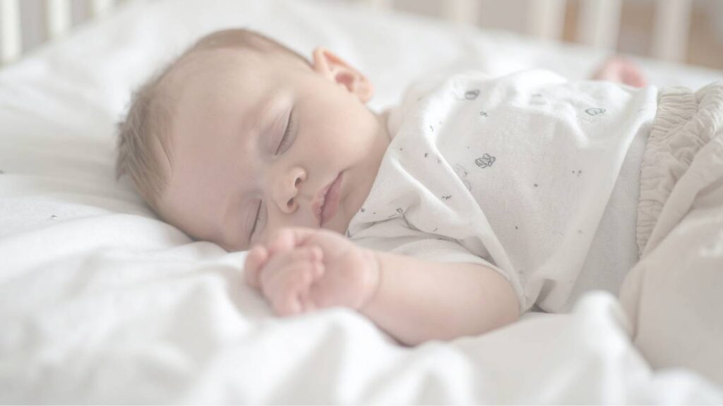 A newborn asleep in a cot with one hand curled up
