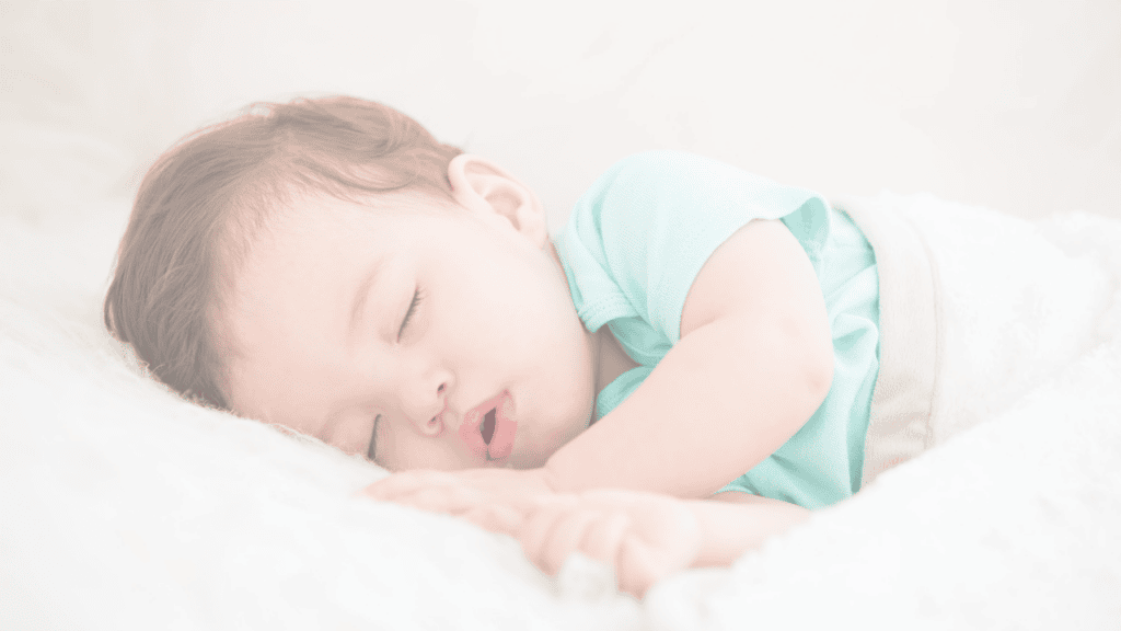 A baby in a mint green top asleep on a white bed