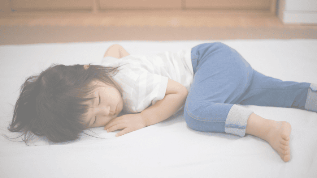 A toddler asleep on their side on a white mattress