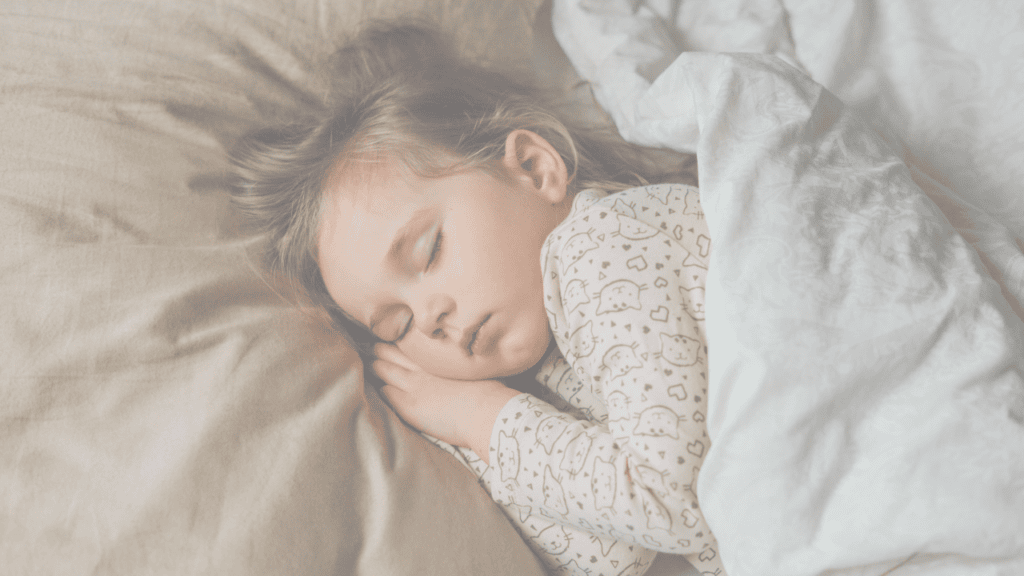 A toddler girl asleep on her side under a grey duvet