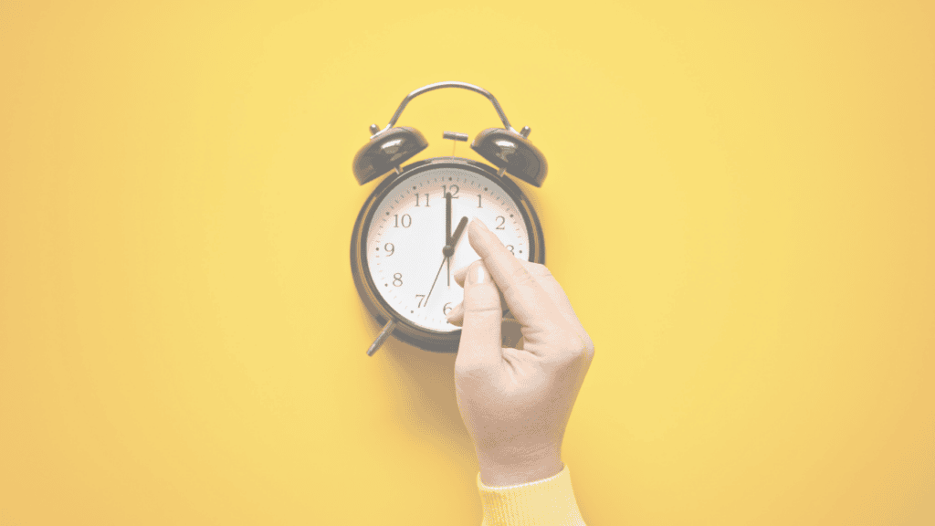 A hand adjusting a black alarm clock against a yellow background