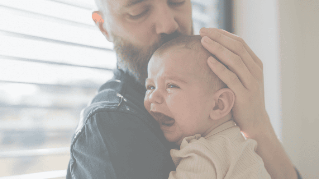 A father comforting a crying baby, with a hand resting gently on the baby's head