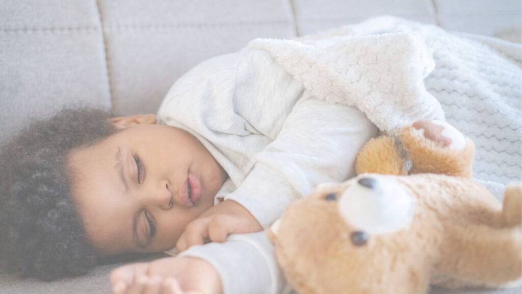 A young child asleep with their arm around a teddy bear