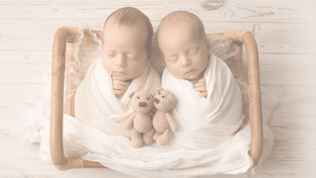 Newborn twins swaddled in cream wraps asleep side by side in a cane crib