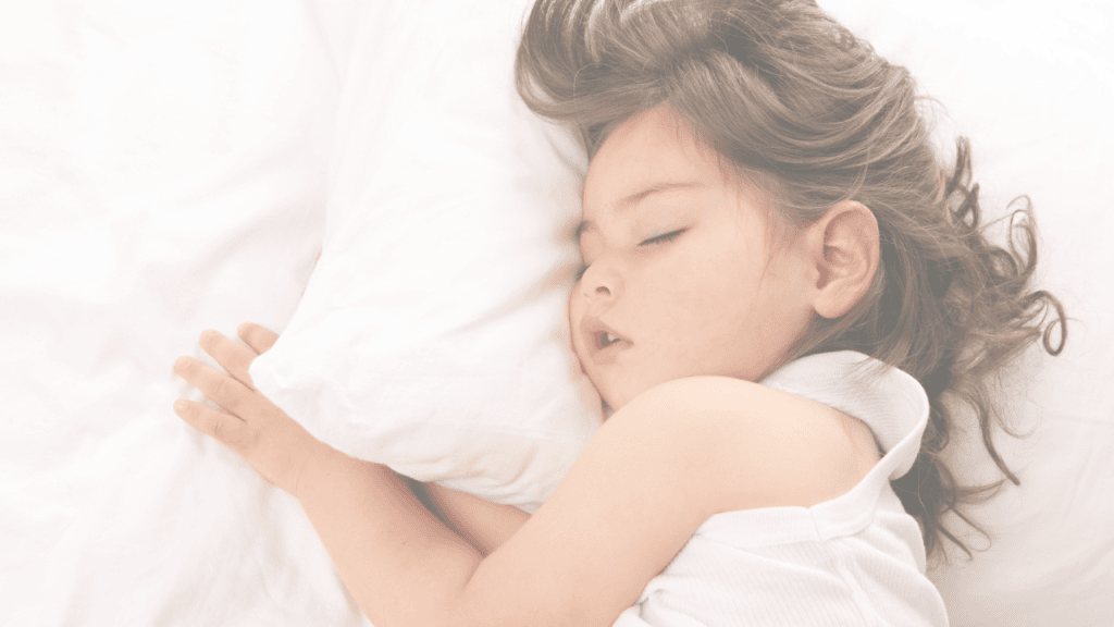 A curly haired toddler girl asleep on a white pillow