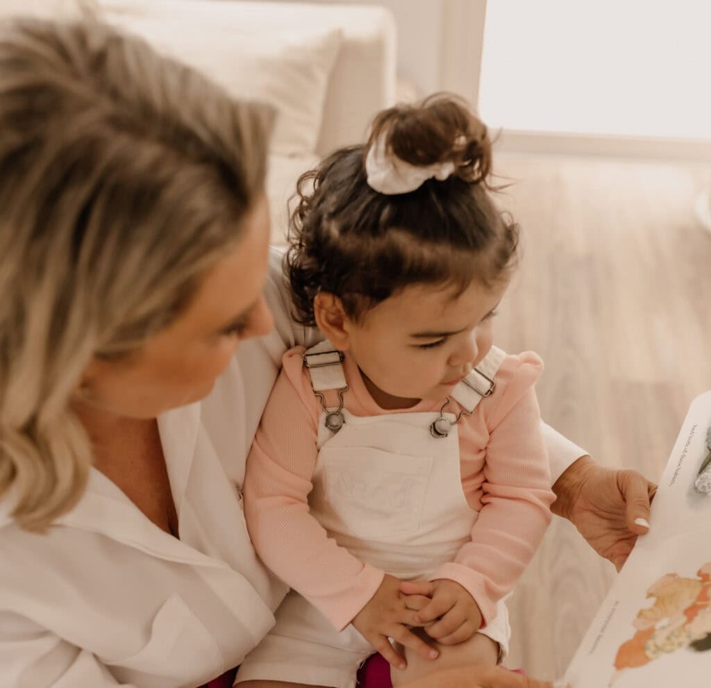 Donna Moala kneeling beside a toddler in a bright room, looking at a picture together