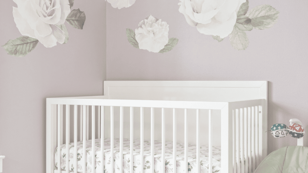 An empty white cot in a nursery with floral wall decals