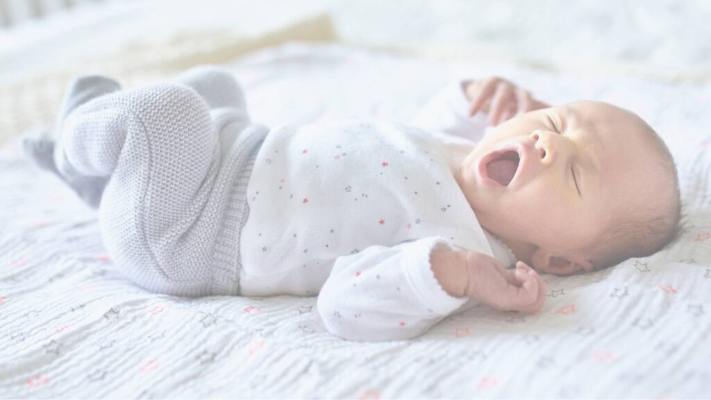 A newborn in a star print onesie yawning on a bed
