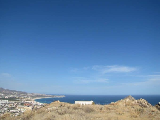 Sweeping View Of Pedregal Coastline With Blue Sky, Ocean, And Hillside Landscape Showcasing Luxurious Pedregal Real Estate In Mexico.