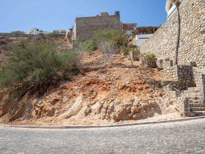 Uneven Rocky Hillside In Pedregal With A Stone Retaining Wall And Stairs, Surrounded By Residential Properties Under Construction On A Sunny Day.