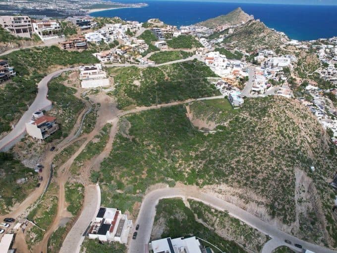 Elevated View Of Pedregal Hillside With Modern Homes, Winding Roads, And Lush Green Terrain Overlooking The Ocean In The Background.