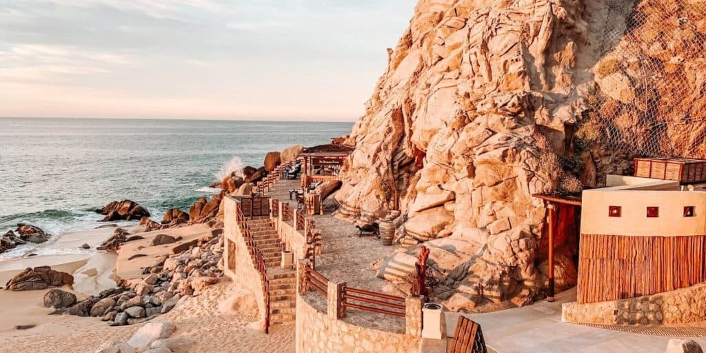 Living In Pedregal Cabo — What Makes This Cliffside Community So Special – Homes For Sale In Pedregal Stunning Pedregal Oceanfront View Showcasing A Private Terrace With Stairs, Rocky Cliffs, And The Expansive Sea In The Background, Capturing The Luxurious Coastal Lifestyle.