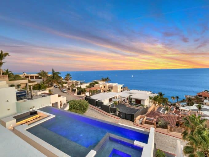 Stunning Pedregal Beachfront View Showcasing Luxury Homes, Infinity Pool, Lush Palm Trees, Vibrant Sunset, And Ocean Horizon, Perfect For Real Estate Investments And Coastal Living.