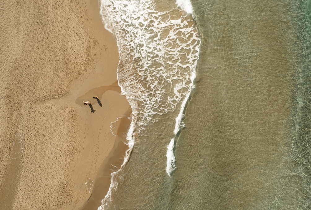 Aerial view of a beach with two people walking along the shoreline.