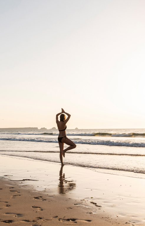 Woman practicing yoga on the beach at sunset in Phuket.
