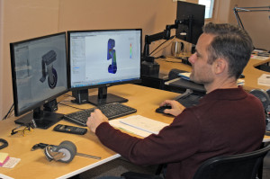 Engineer working on caster design with dual monitors at desk.