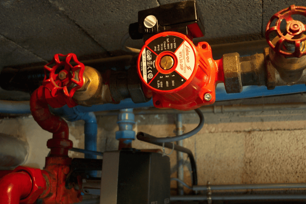 A red Salmson circulation pump installed on a pipe with manual shut-off valves, typical of a boiler repair setup.