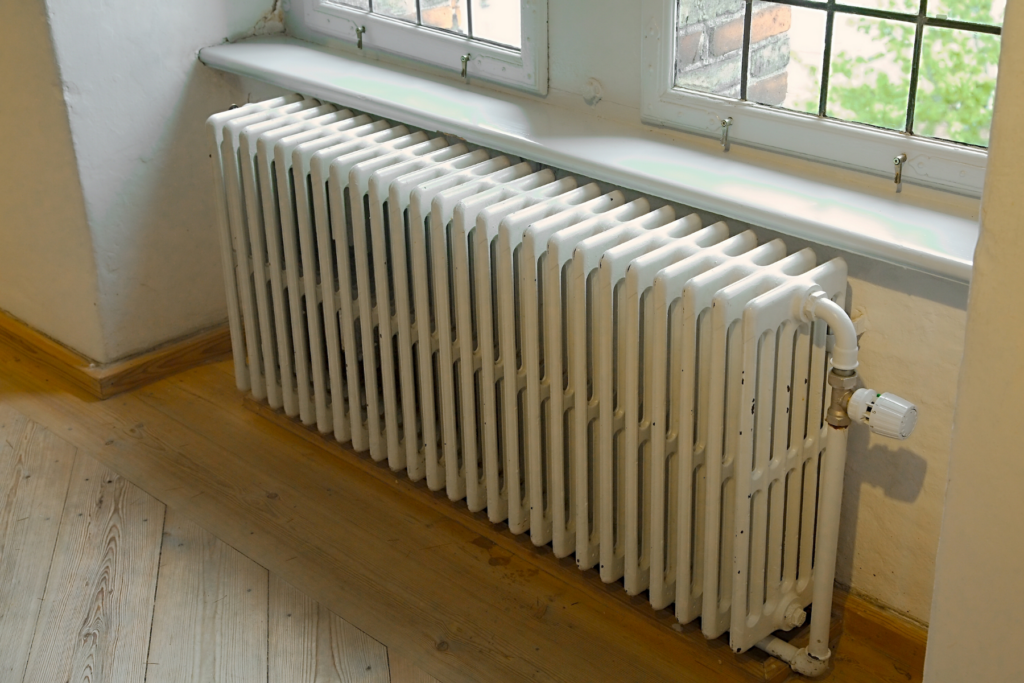 White cast iron radiator beneath a window that is cold and requires radiator troubleshooting.