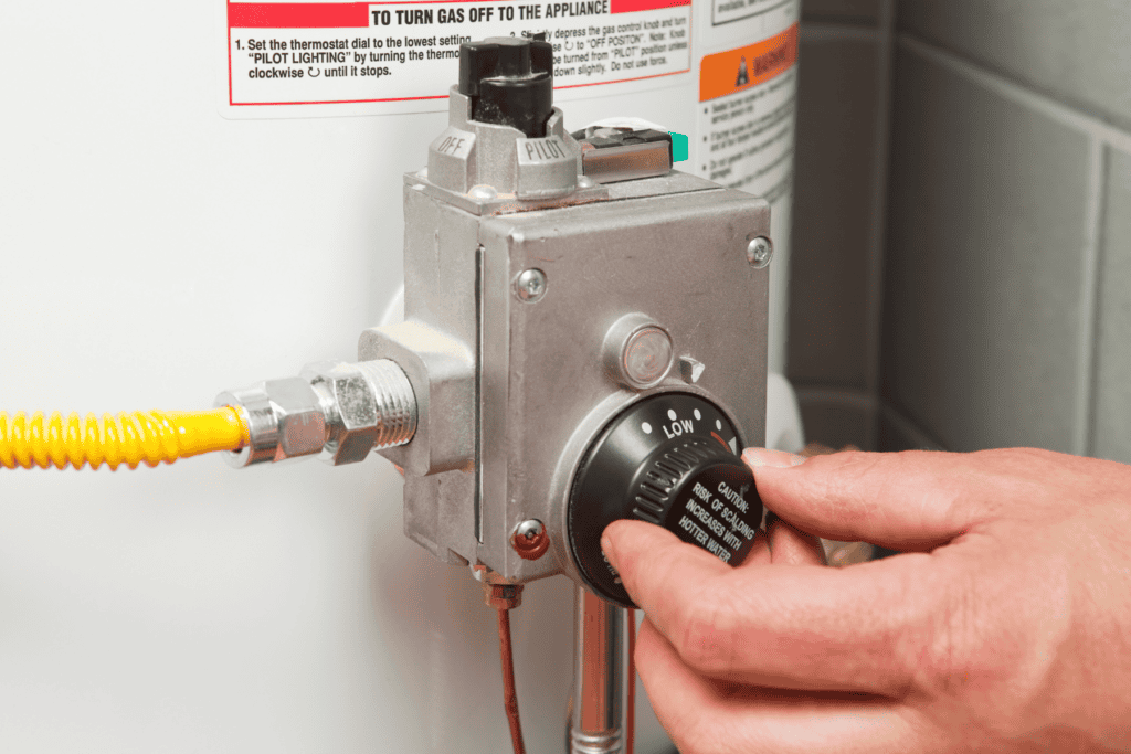 A person adjusting the temperature setting on a home water heater gas control valve.