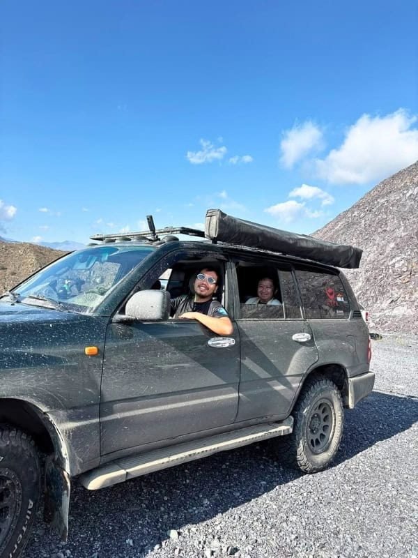 Traveler sitting in a rugged 4x4 vehicle during an off-road adventure through rocky mountains.