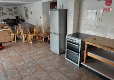Empty kitchen with stove, refrigerator, stacked chairs.