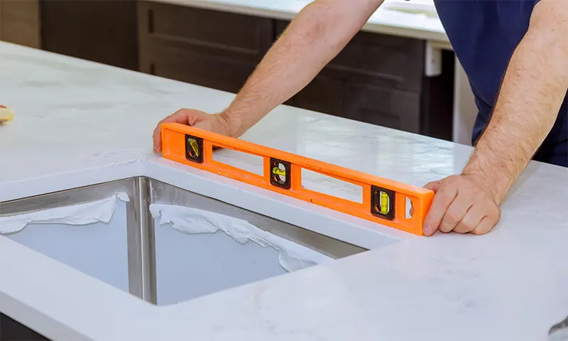 Person leveling kitchen countertop with orange spirit level.
