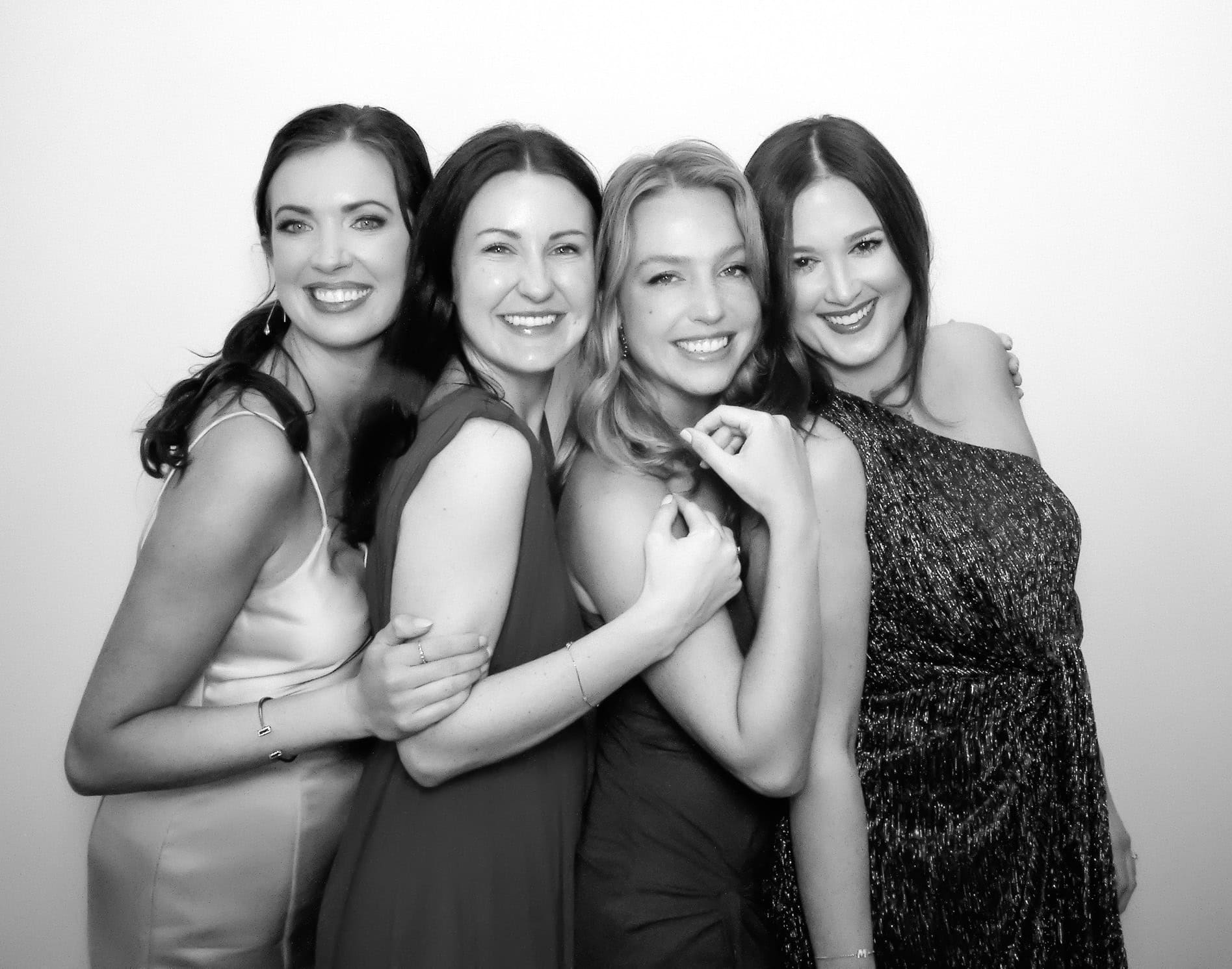 Group of four women smiling and having fun at a photo booth, black and white image.