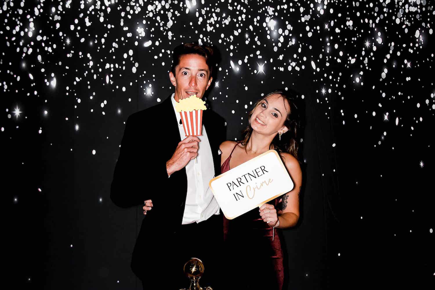 Happy couple at a photo booth with confetti backdrop, celebrating a special event.