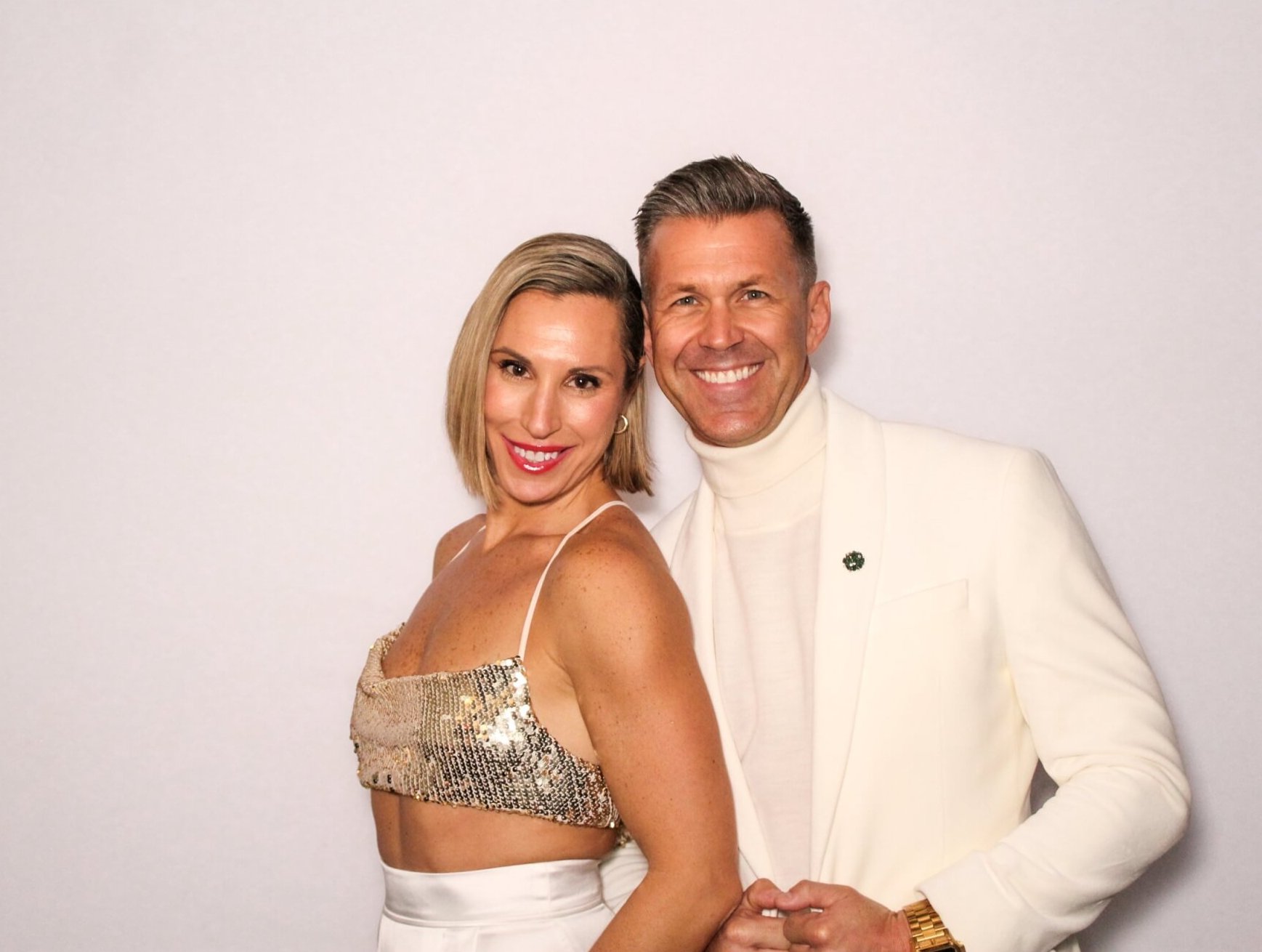 Elegant couple at a photo booth event, smiling and dressed stylishly.