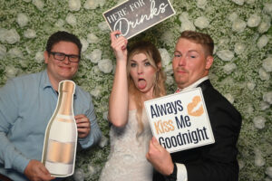 Bride and Groom with guest at wedding photo booth hd holding playful signs and props.