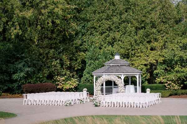 Elegant outdoor wedding gazebo with white drapery and floral decorations in a lush green park setting.